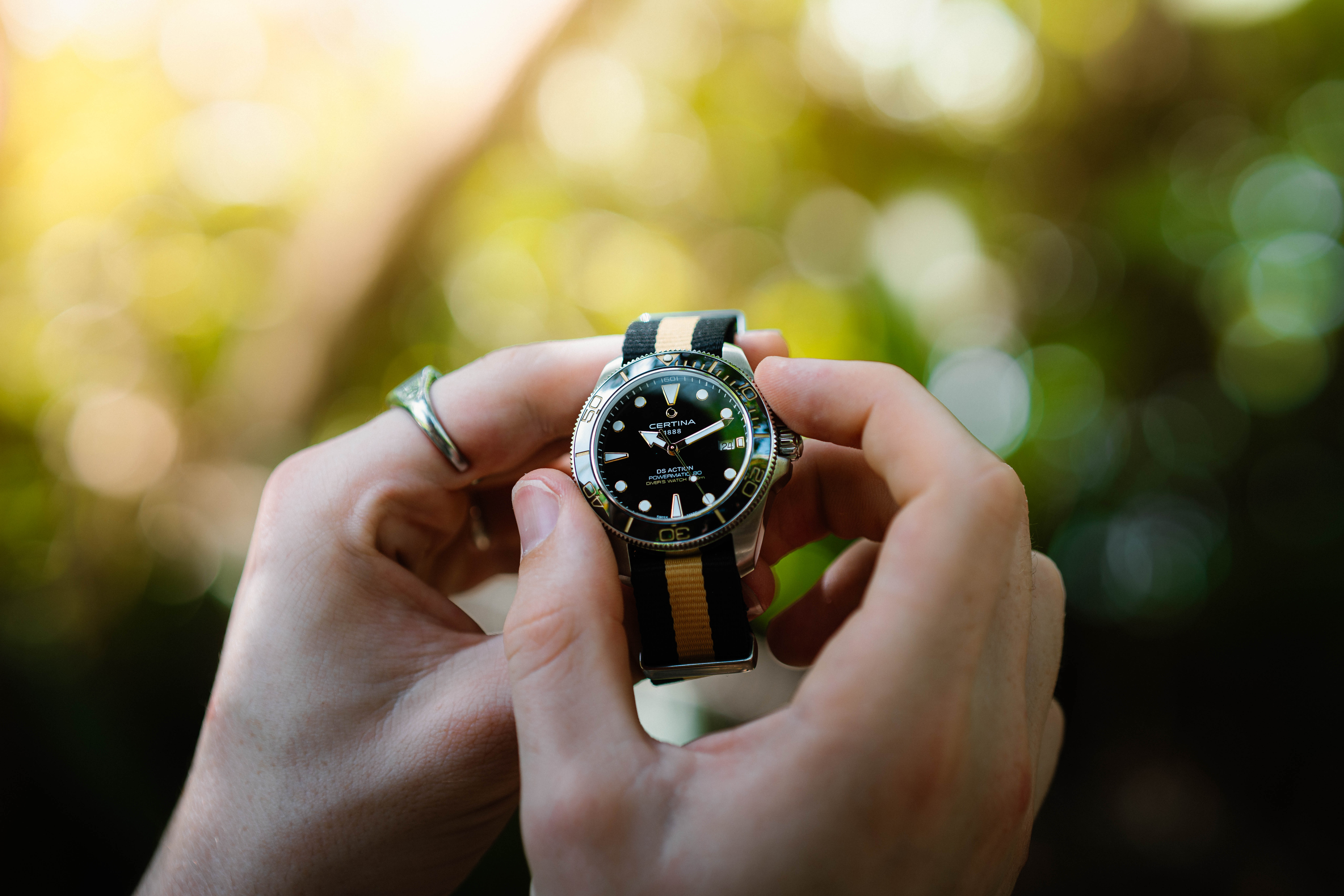 Two hands holding a watch with a black and brown strap